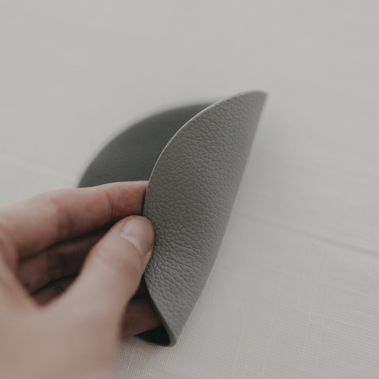 Hand biegt wendbaren grauen Untersetzer, zeigt flexible und strukturierte Materialoberfläche.