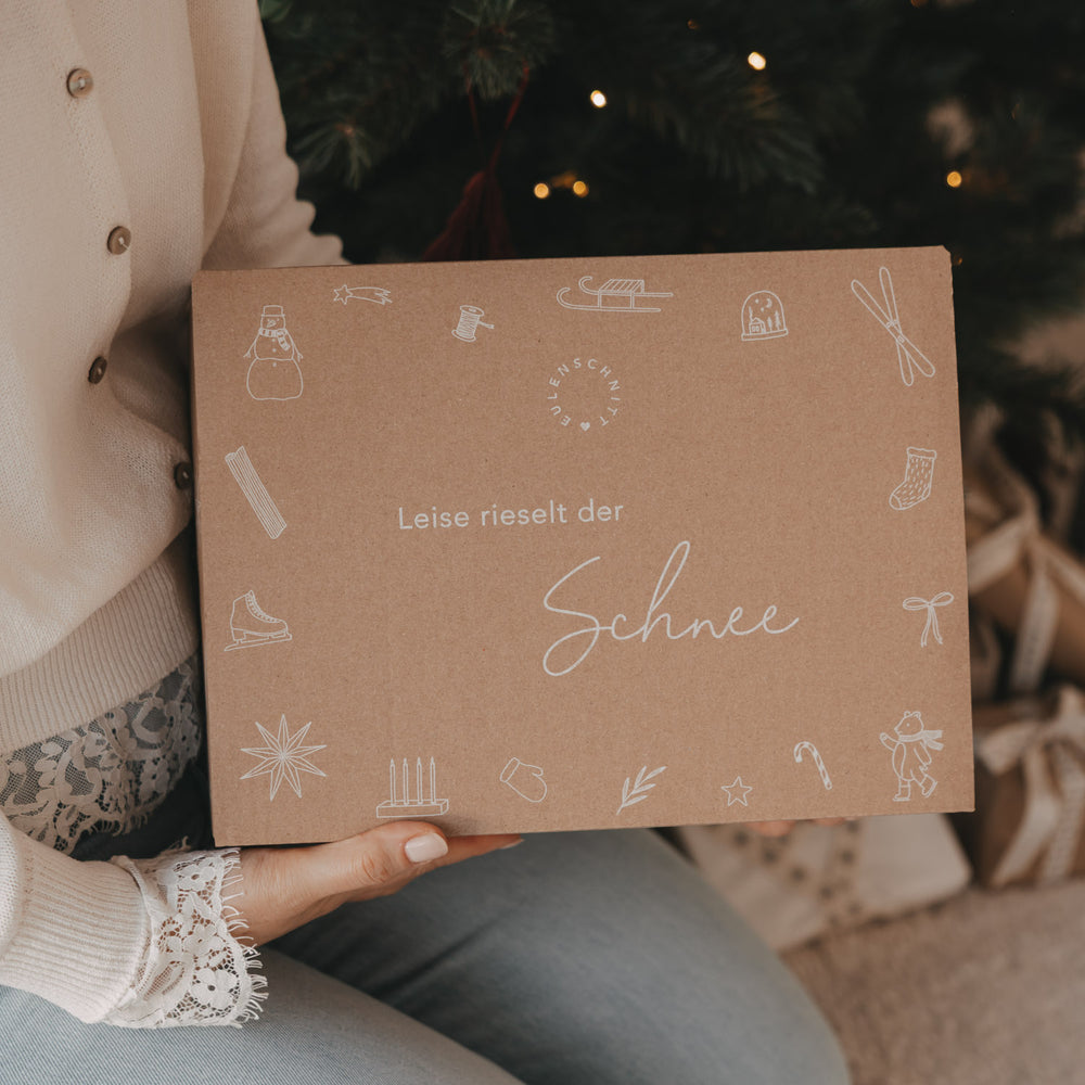 Nahaufnahme der limitierten Winter-Überraschungsbox 2026 von Eulenschnitt mit weißen Weihnachts- und Winterillustrationen auf naturbraunem Karton.