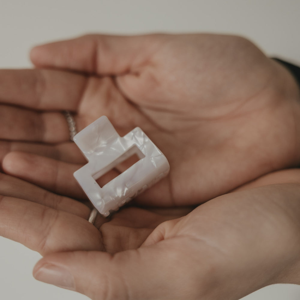 Kleine eckige Haarspange in Perlmutt-Optik in der Hand präsentiert