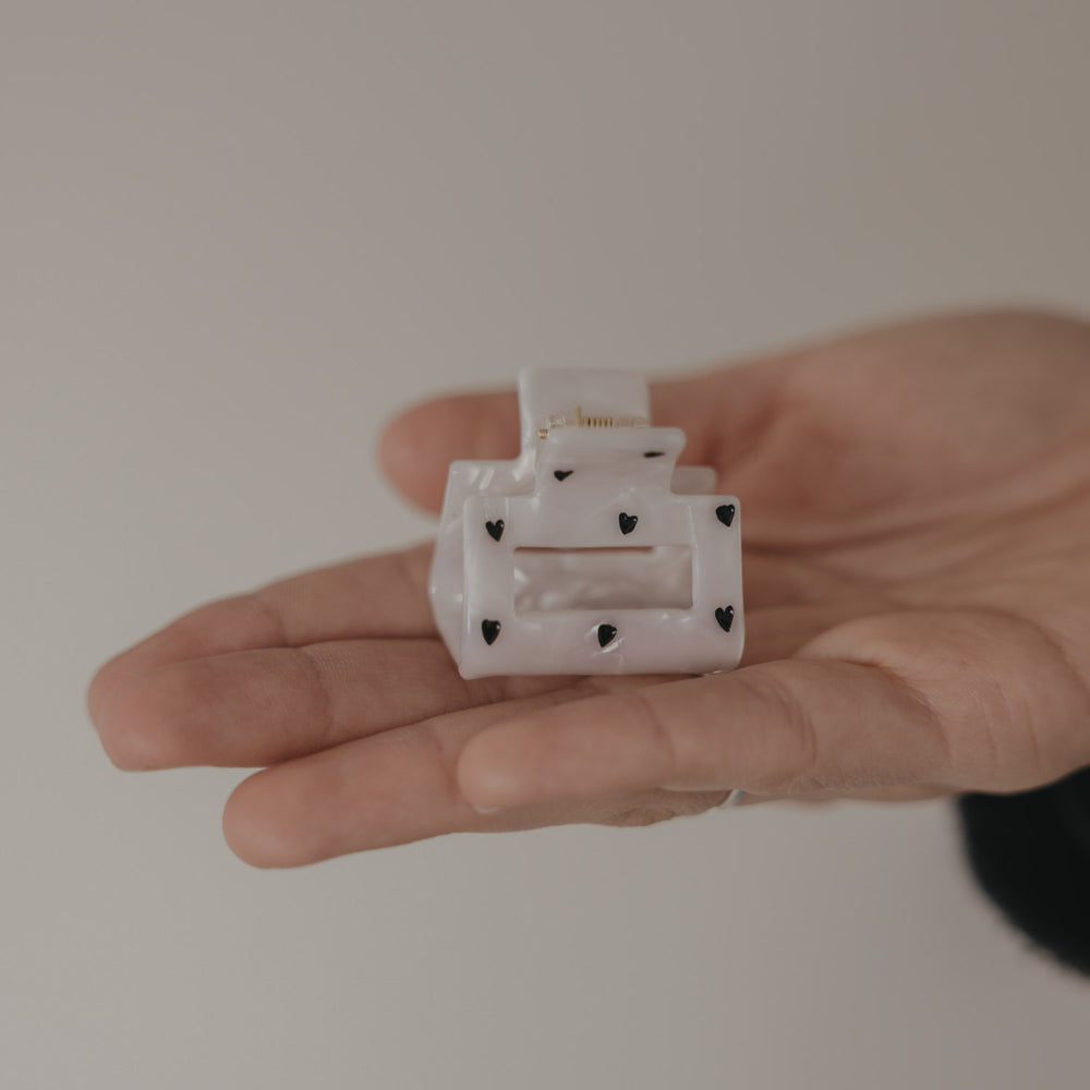 Kleine eckige Haarspange in Perlmutt-Optik mit schwarzen Herzen in der Hand präsentiert