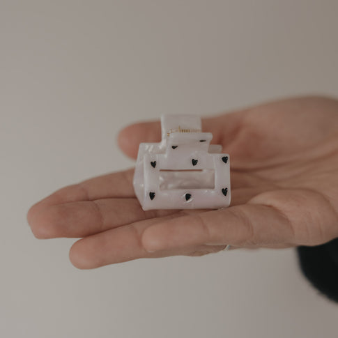 Kleine eckige Haarspange in Perlmutt-Optik mit schwarzen Herzen in der Hand präsentiert