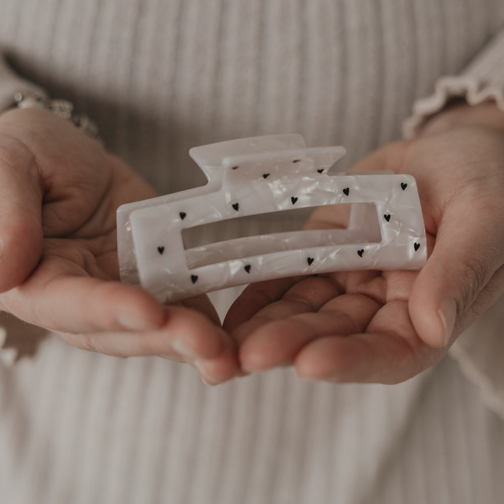 Maxi eckige Haarspange mit schwarzen Herzen in Perlmutt-Optik in den Händen präsentiert
