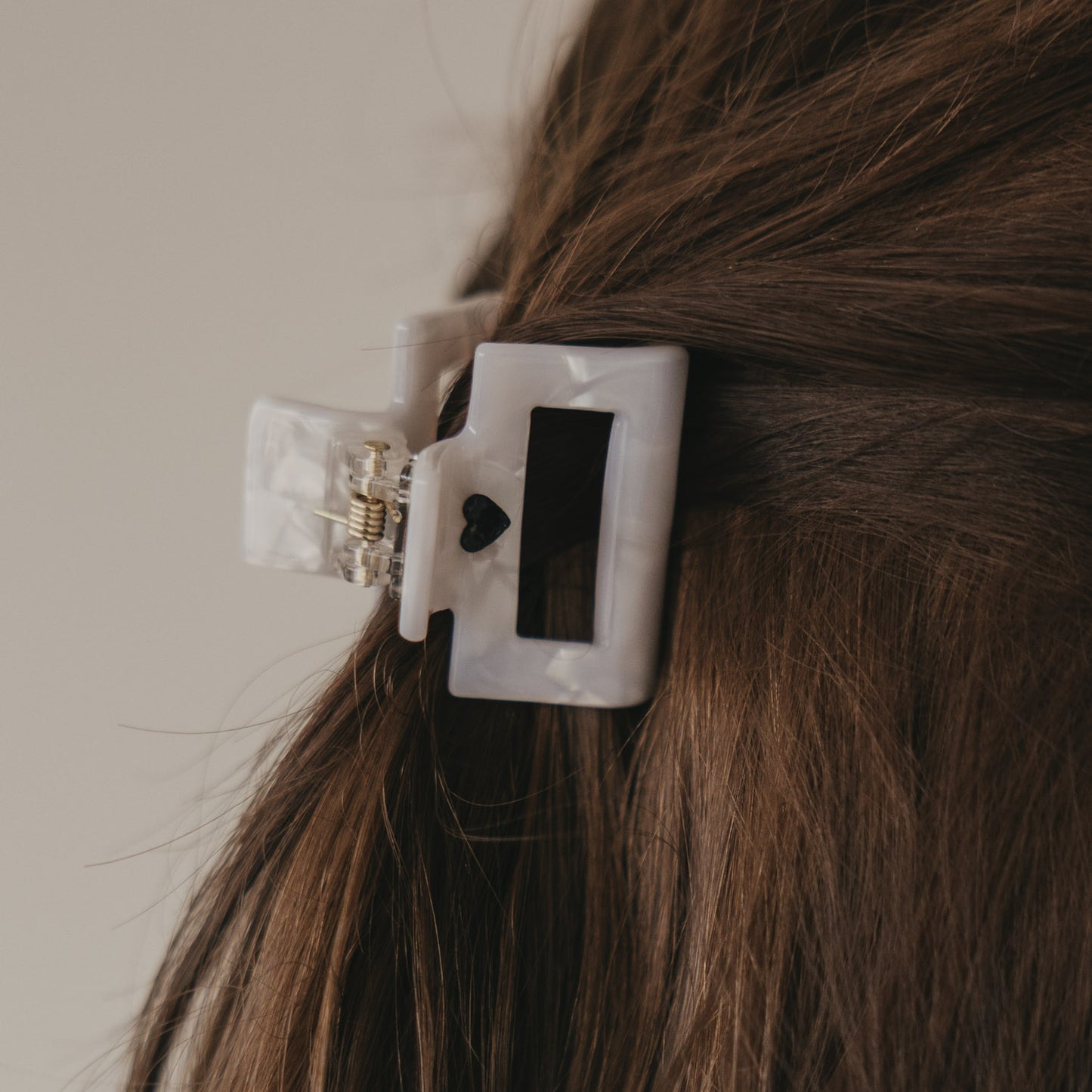 Kleine eckige Haarspange in Perlmutt-Optik mit schwarzem Herz im halboffenen Haar