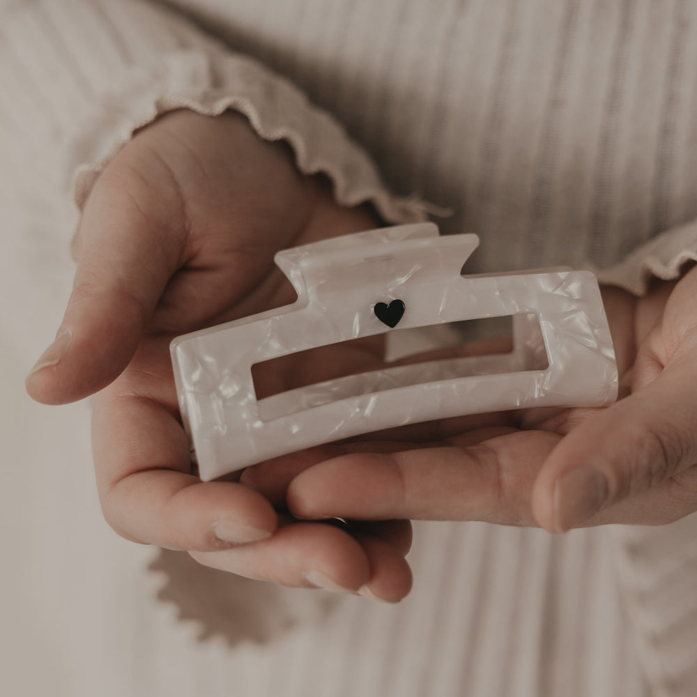 Maxi eckige Haarspange in Perlmutt-Optik mit schwarzem Herz in der Hand präsentiert