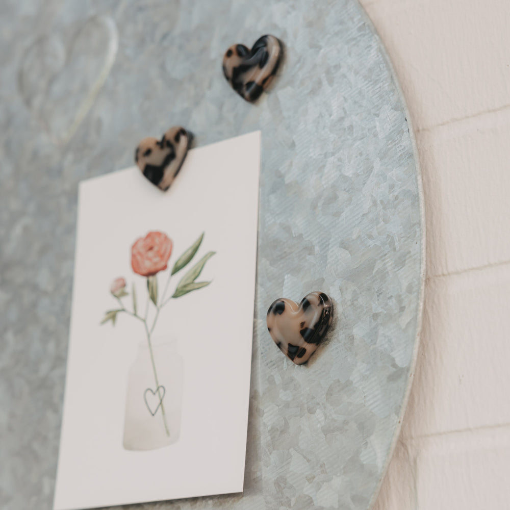 Herzmagnete im Leo-Look befestigen eine Blumenkarte an einer magnetischen Pinnwand