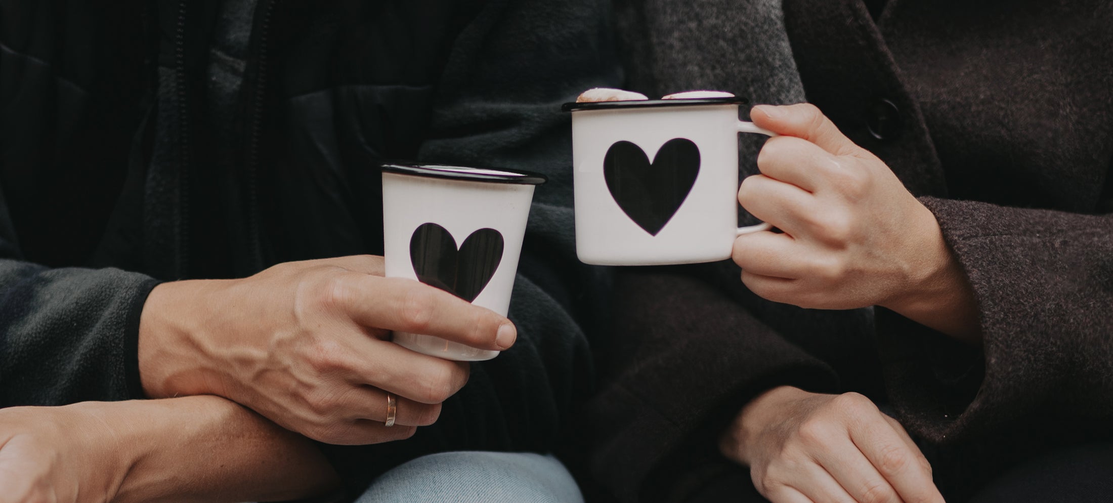 Zwei Personen halten Emaillebecher mit schwarzem Herzmotiv in den Händen. Text im Bild: „Für jedes Abenteuer – Emaille-Geschirr.“