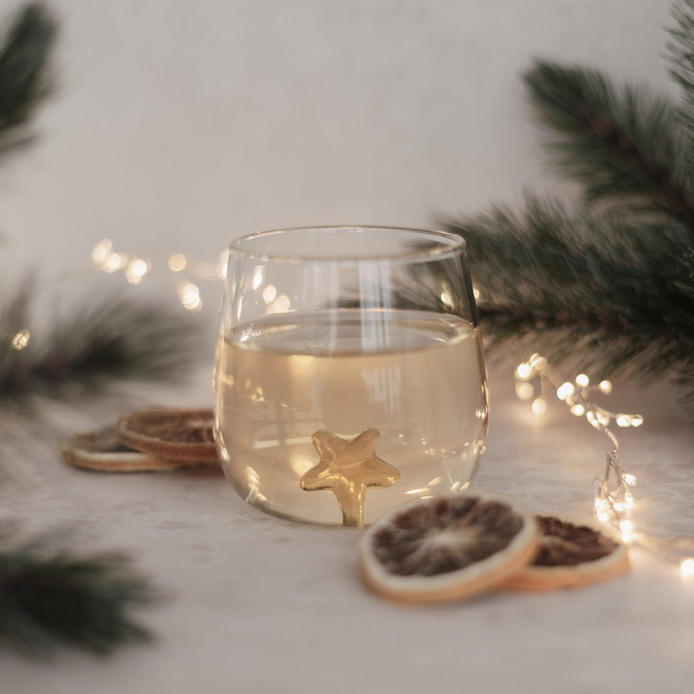 Trinkglas mit goldener Sternfigur im Boden, festlich dekoriert mit getrockneten Orangenscheiben und Tannenzweigen