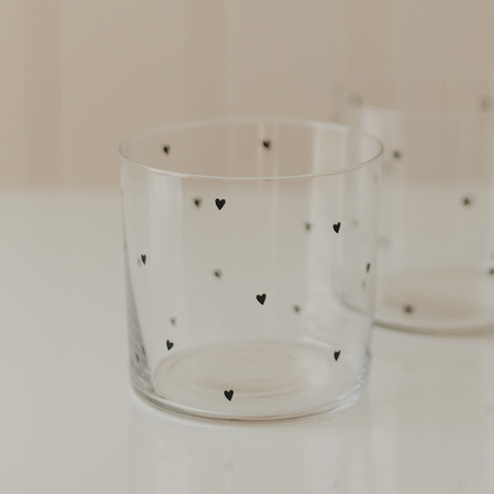 Transparentes Trinkglas mit kleinen schwarzen Herzen, im Hintergrund ein zweites passendes Glas