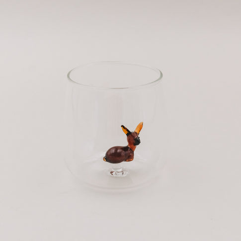 Trinkglas mit Rehfigur aus braunem Glas auf hellem Hintergrund – das Reh steht zentriert im Glas.