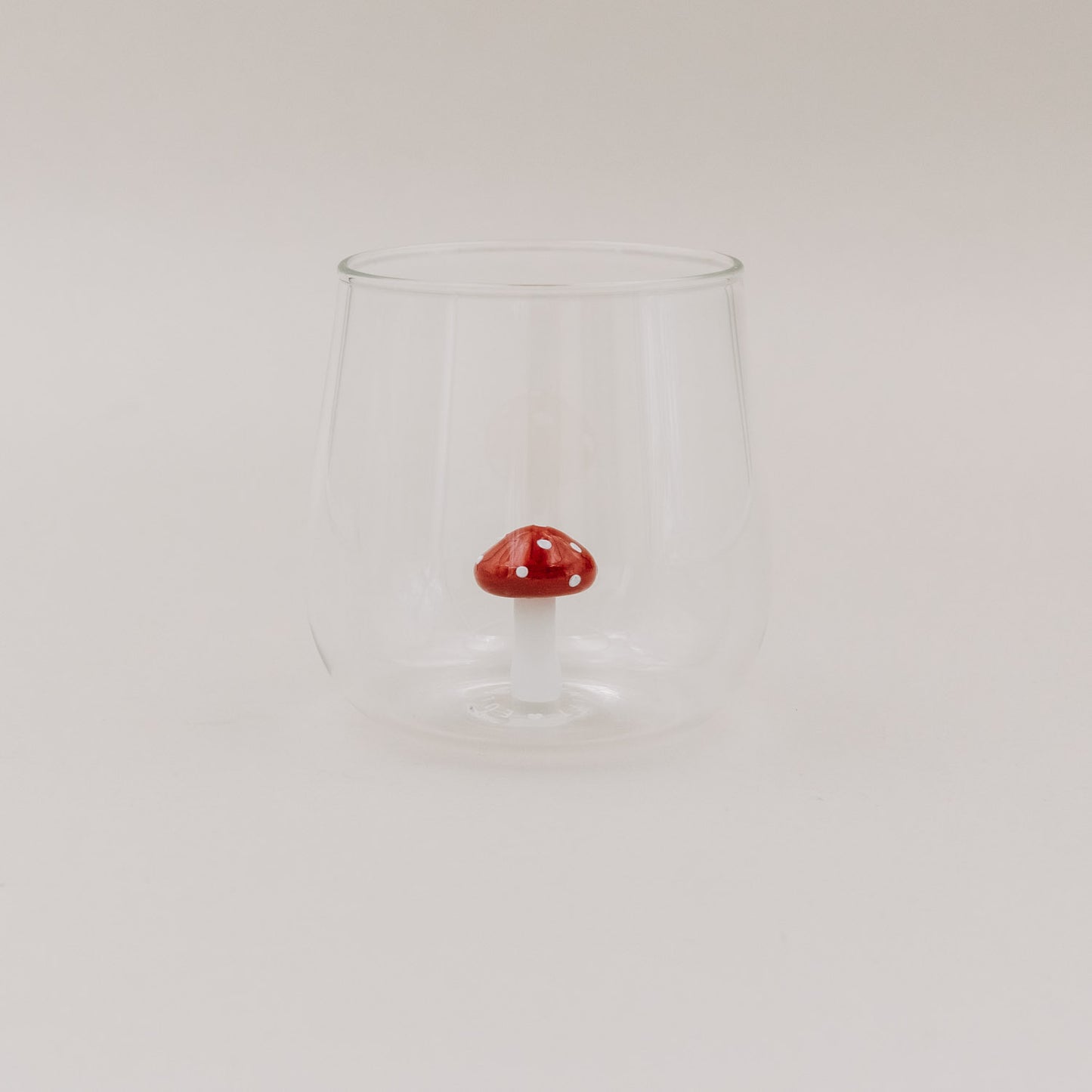 Trinkglas mit roter Pilzfigur auf hellem Untergrund – minimalistisches Design mit 3D-Fliegenpilz im Inneren