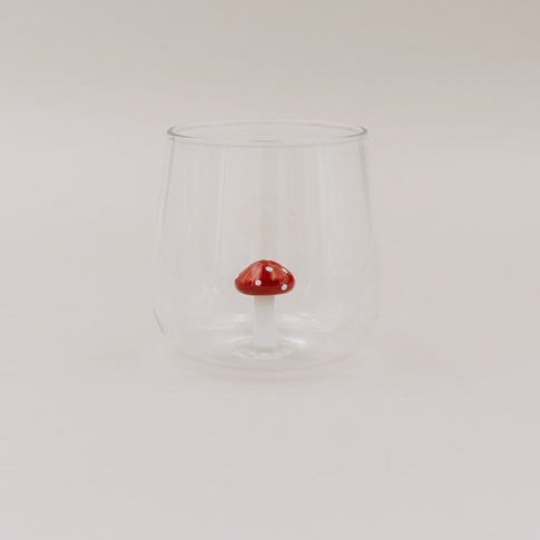 Trinkglas mit roter Pilzfigur auf hellem Untergrund – minimalistisches Design mit 3D-Fliegenpilz im Inneren