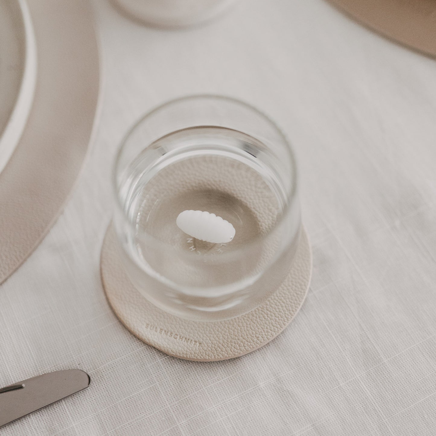 Draufsicht auf Trinkglas mit Muschelmotiv am Boden auf strukturiertem Untersetzer