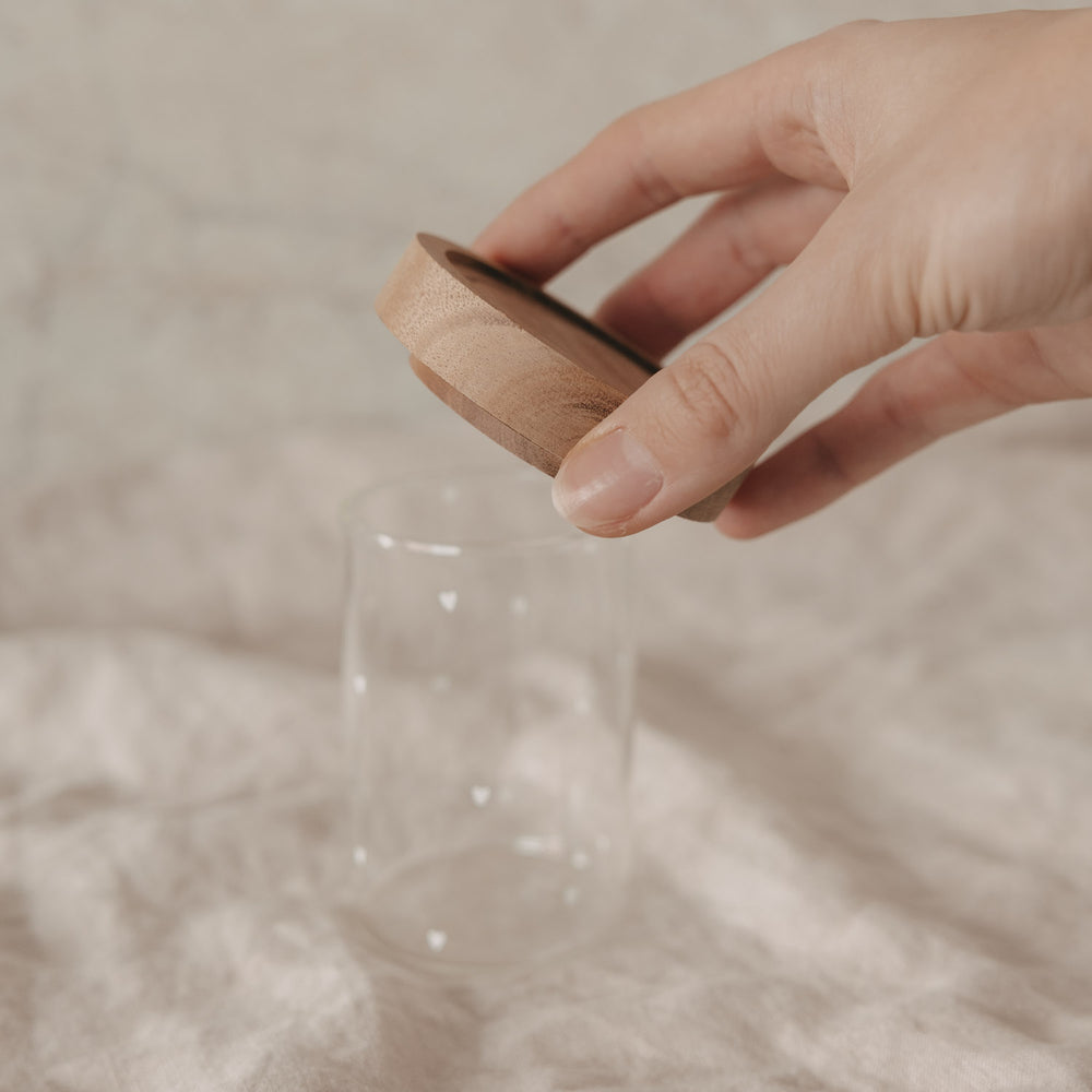 Hand setzt Holzdeckel auf kleines Vorratsglas mit weißen Herzen