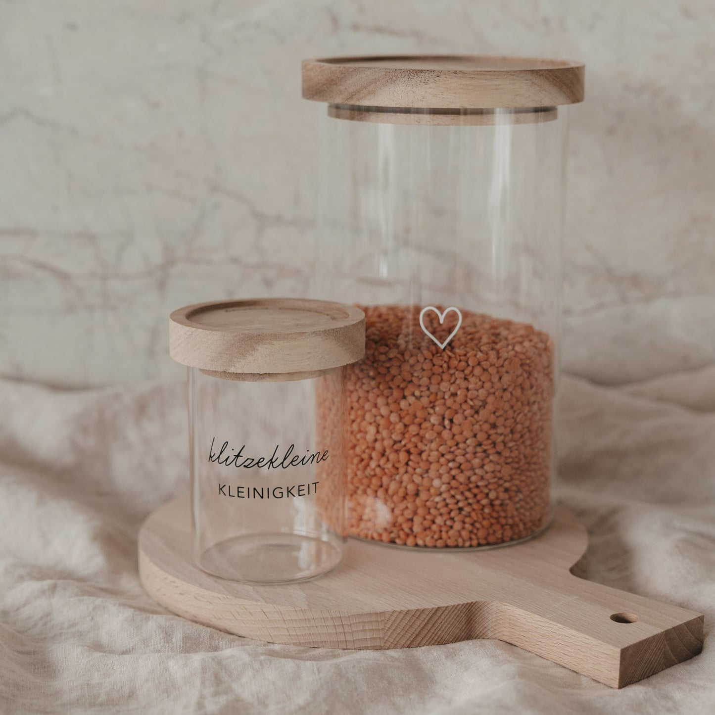 Minivorratsglas „klitzekleine Kleinigkeit“ neben großem Vorratsglas mit Herzmotiv auf Holzbrett