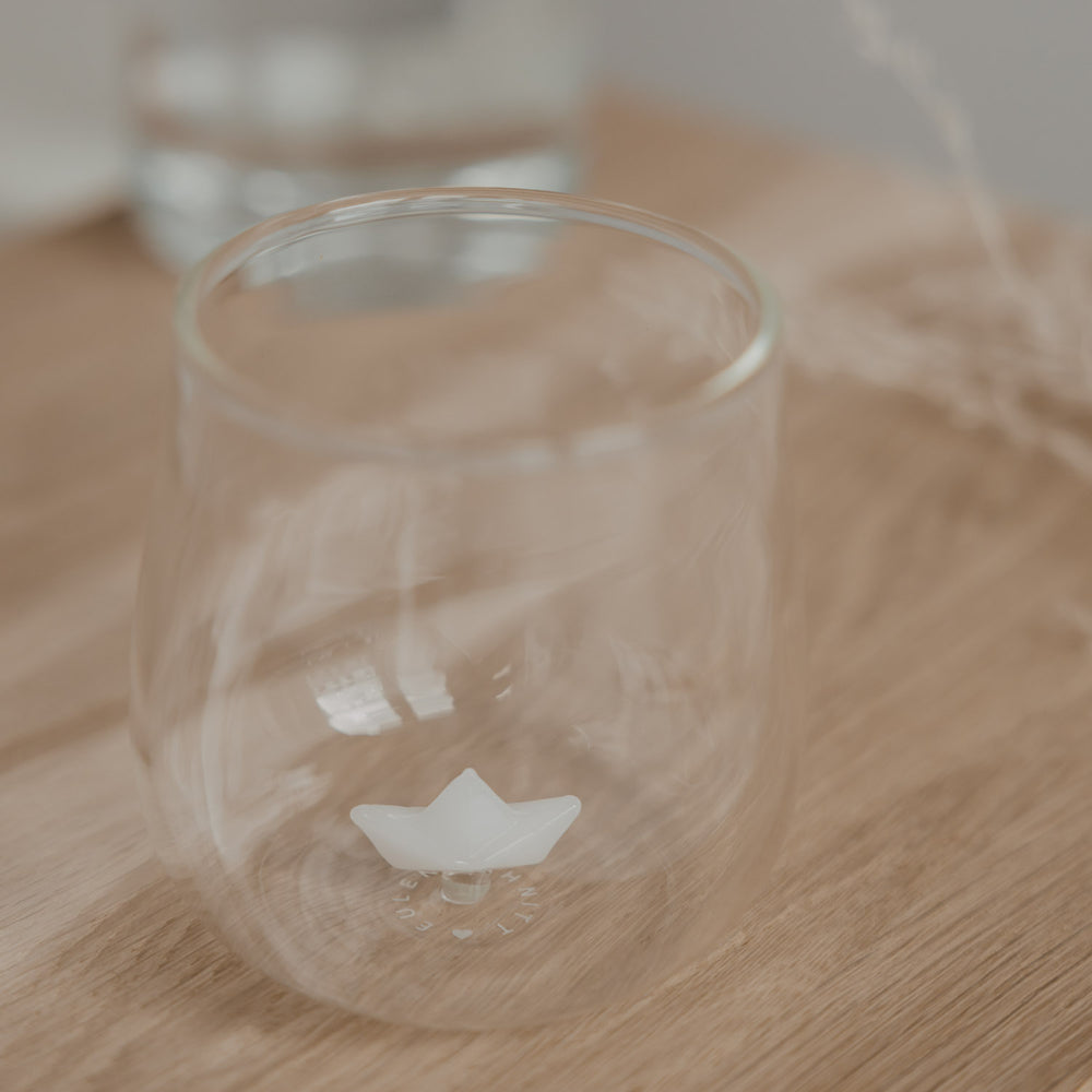 Minimalistisches Trinkglas mit Papierboot Design auf Holzbrett, stilvolles Glas für Getränke