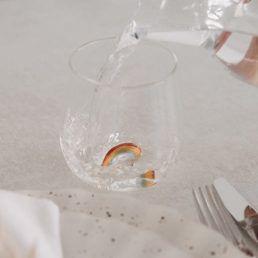 Transparentes Glas mit Regenbogen-Design wird mit Wasser befüllt, modernes Doppelwandglas auf gedecktem Tisch
