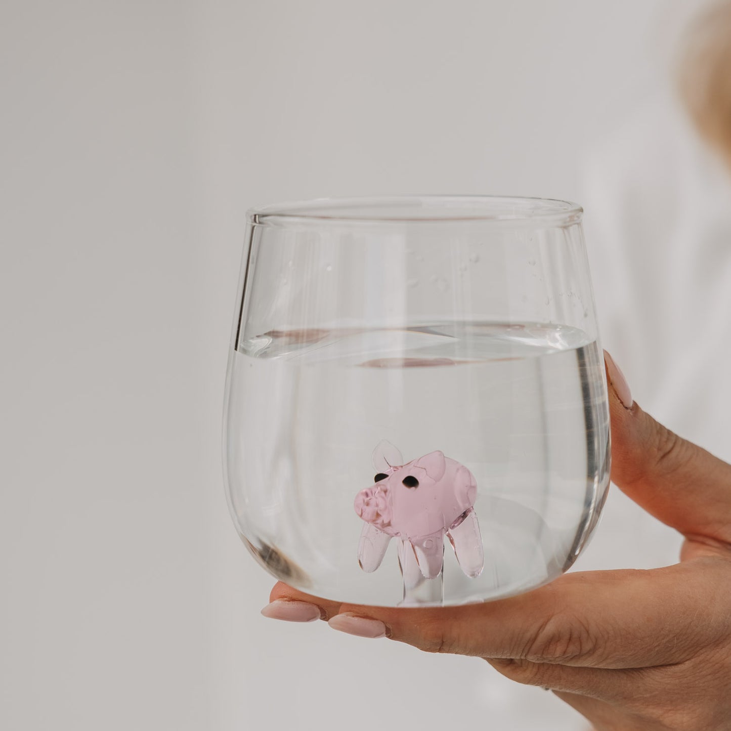 Trinkglas mit rosa Schwein im Boden, in der Hand gehalten, klares Glasdesign