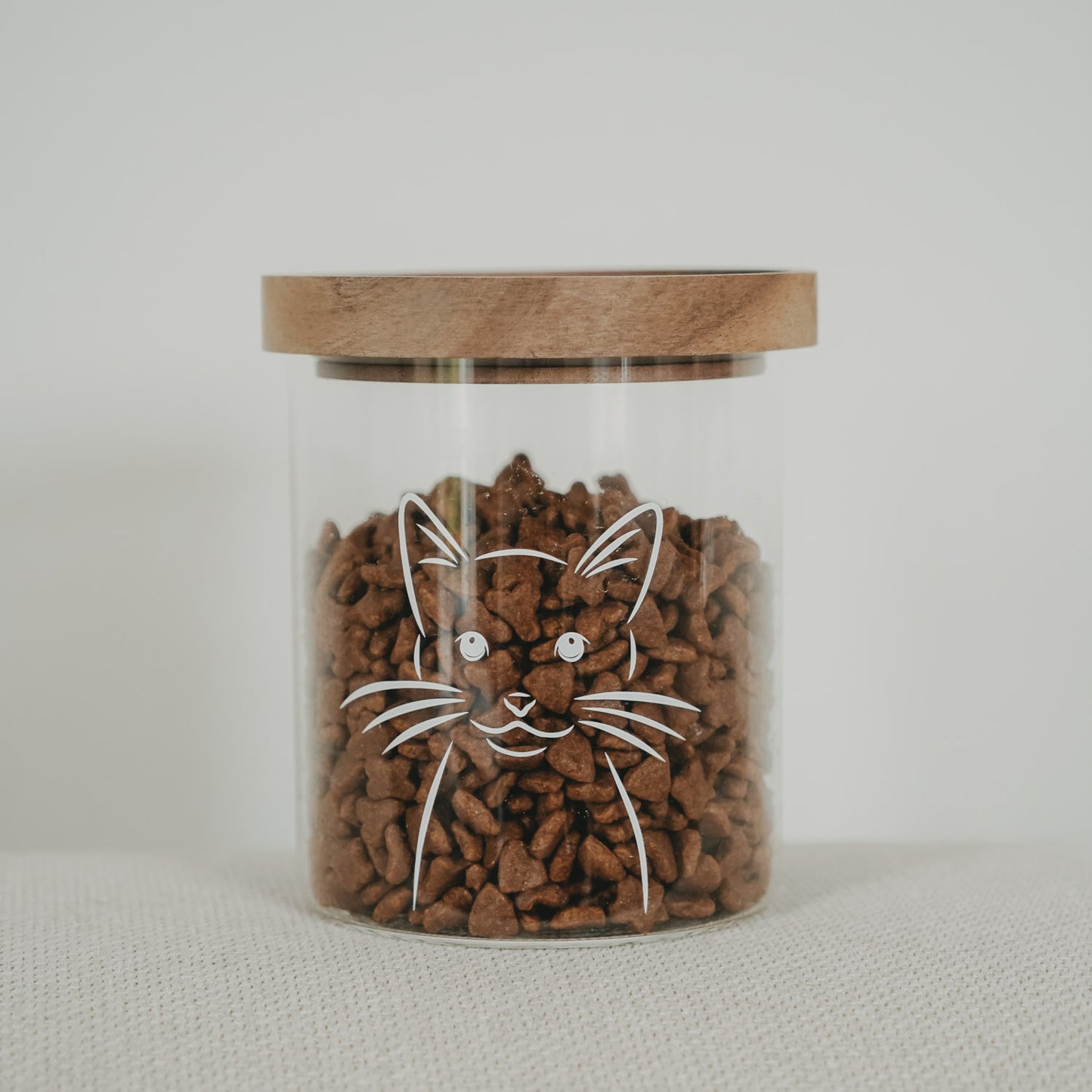 Vorratsglas mit weißem Katzenmotiv, Holzdeckel und Trockenfutter als freigestellte Produktaufnahme.