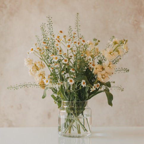 Glasvase mit Blumen auf hellem Tisch, dekorativ und natürlich inszeniert