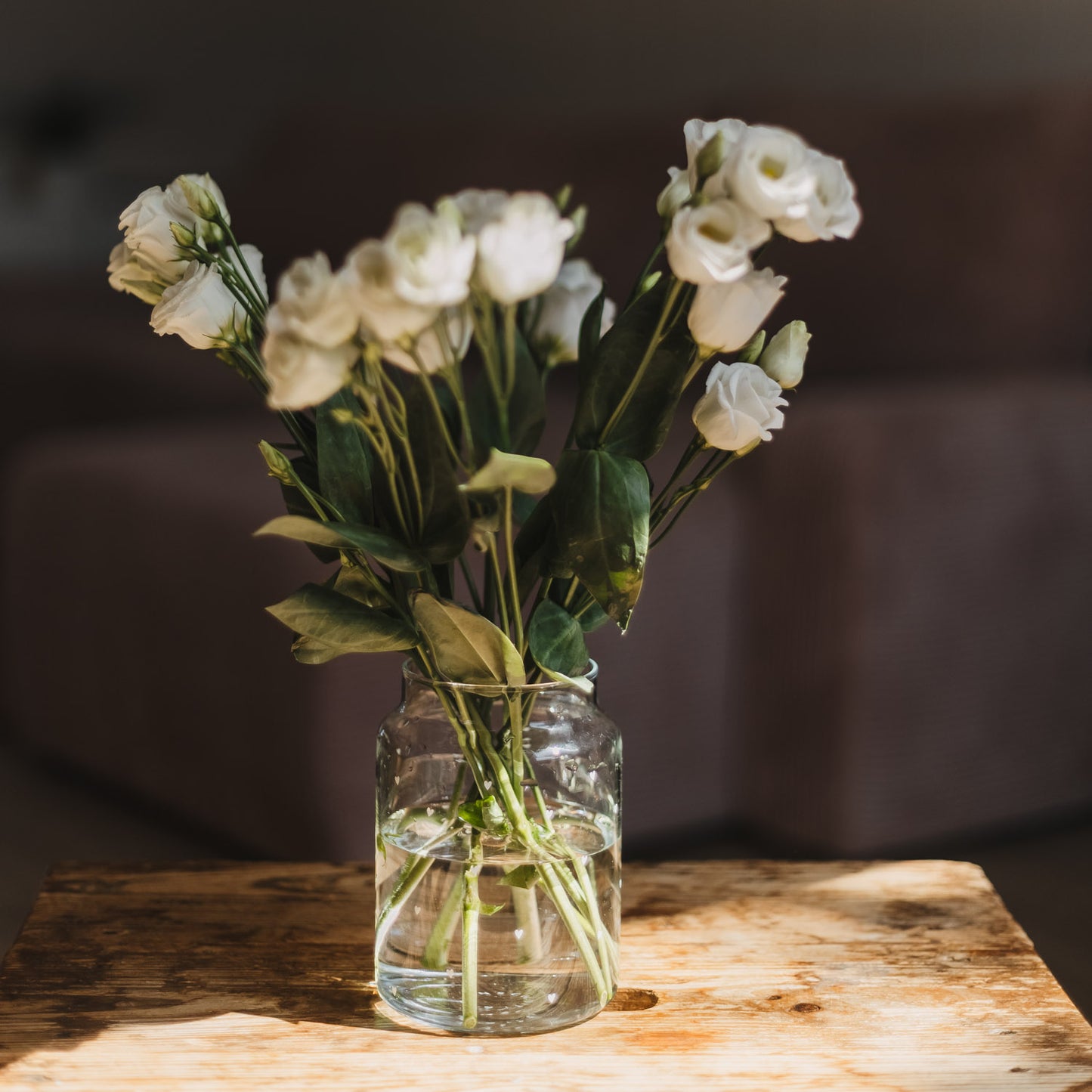 Glasvase mit weißen Blumen im warmen Licht auf rustikalem Holztisch
