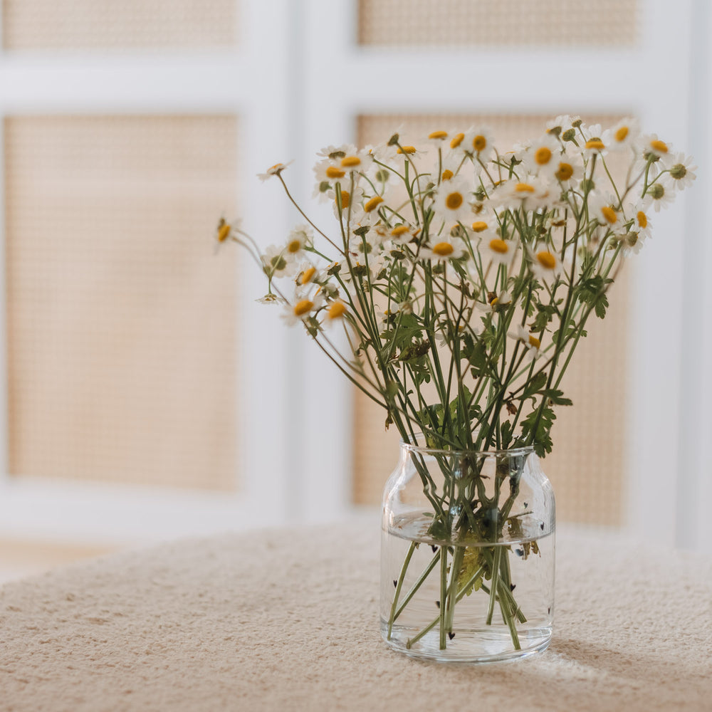 Glasvase mit Herzmuster als Deko mit Blumen auf hellem Tisch