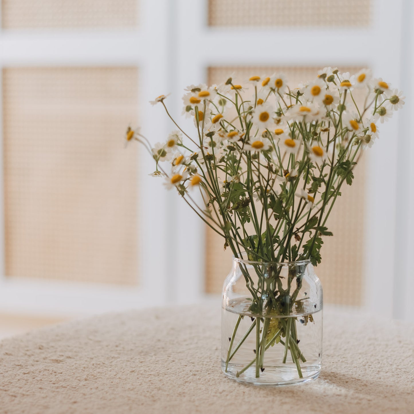 Glasvase mit Herzmuster als Deko mit Blumen auf hellem Tisch