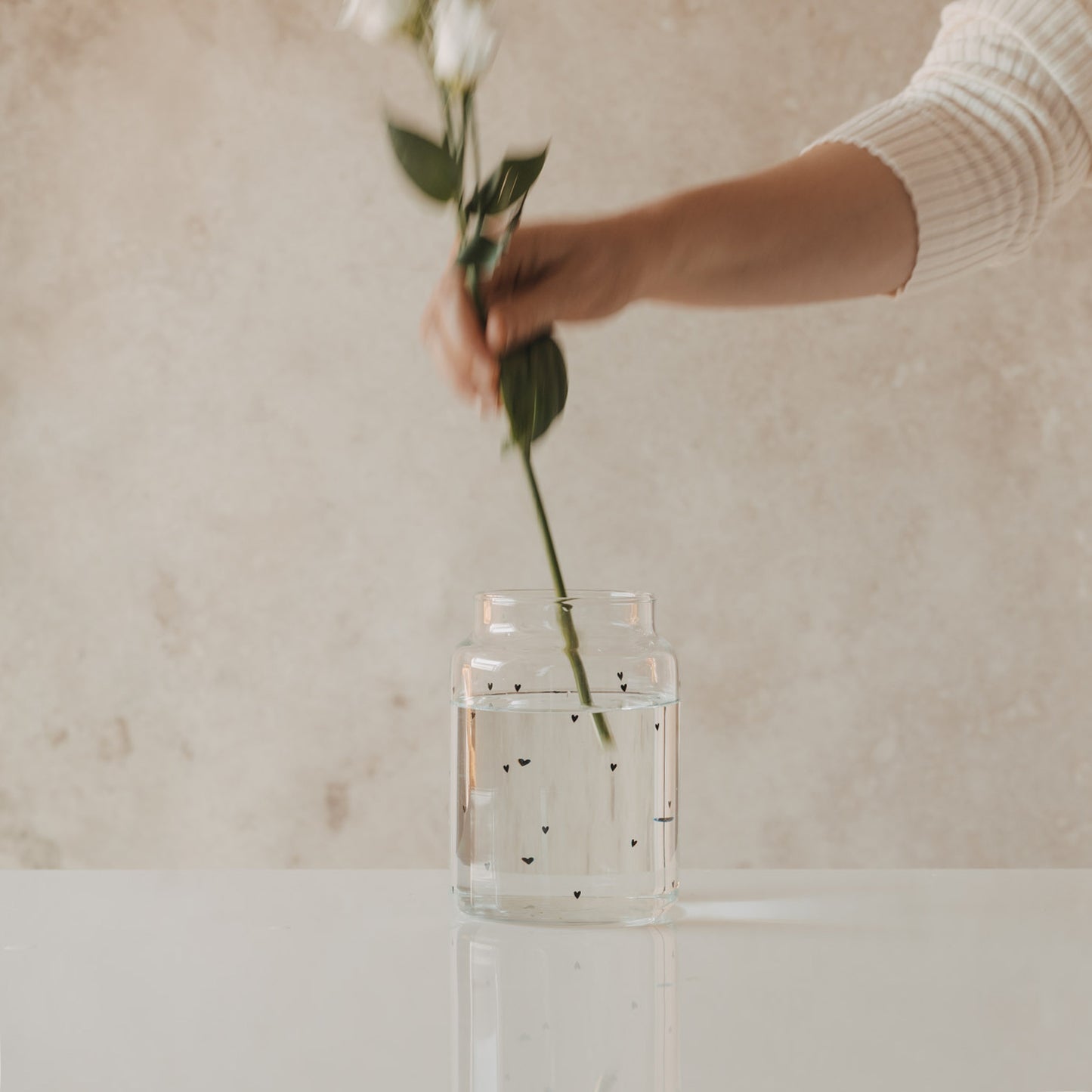 Glasvase mit schwarzen Herzen beim Arrangieren von Blumen