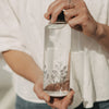 Detail Glas Trinkflasche mit Blumenmotiv, in der Hand gehalten, filigranes Design