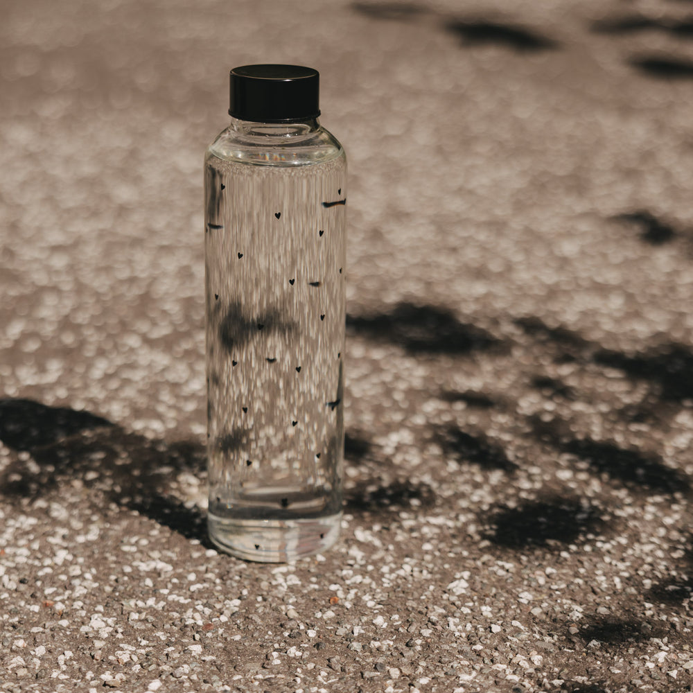 Glas Trinkflasche mit Herzmuster draußen im Sonnenlicht, schlicht und modern