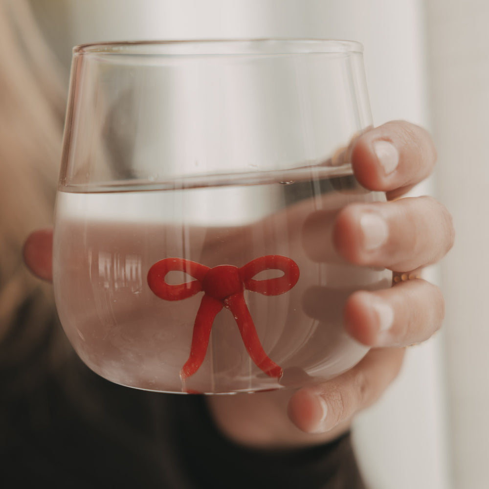 Nahaufnahme eines transparenten Trinkglases mit roter Schleifenfigur im Glasboden, gefüllt mit Wasser.