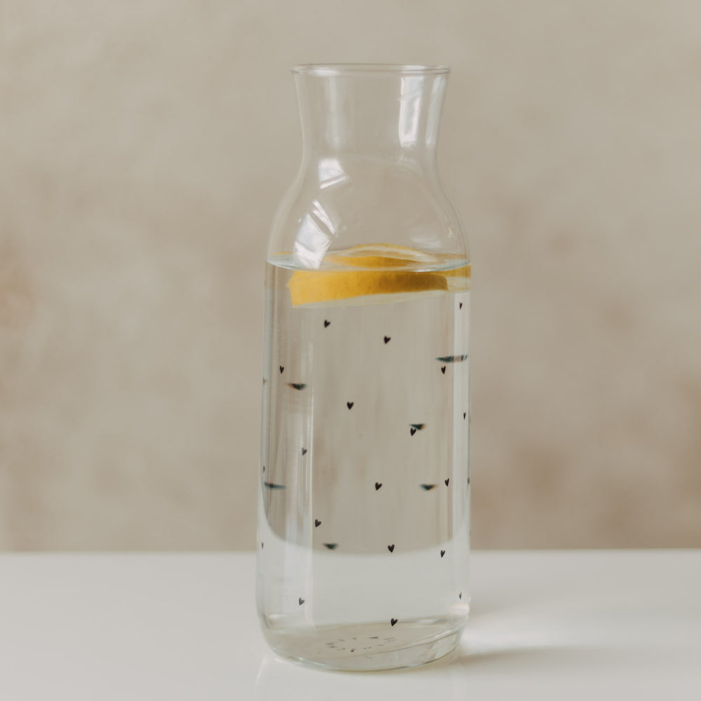 Glaskaraffe mit schwarzem Herzmuster, Wasser und einer Zitronenscheibe
