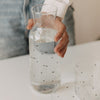 Hand hält eine mit Wasser gefüllte Glaskaraffe mit kleinen schwarzen Herzen