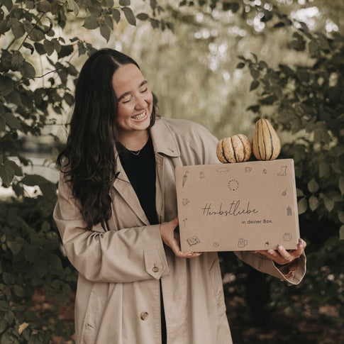 Frau hält Herbstbox mit Kürbissen im Freien, Geschenkidee für den Herbst mit Naturdeko und liebevoller Verpackung.