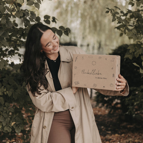 Frau im Laub und hält die Herbstbox mit herbstlichen Motiven, ideales Geschenk für die gemütliche Jahreszeit.