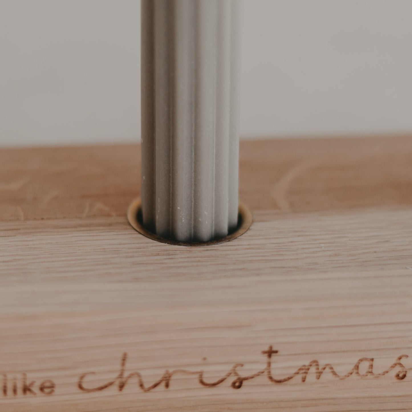 Nahaufnahme grauer Kerze im Holzkerzenhalter mit feiner Gravur Christmas