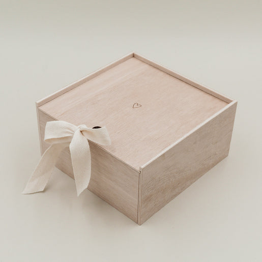 Erinnerungsbox Herz aus Holz mit Schleifenband geschlossen, minimalistisch vor hellem Hintergrund.