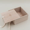 Offene Erinnerungsbox aus Holz mit herausgezogener Schiebeklappe und cremefarbener Schleife.