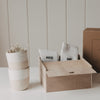 Erinnerungsbox aus Holz mit drei eingravierten Herzen und Herz-Ausschnitt, gefüllt mit „Mr“ und „Mrs“-Socken. Daneben stehen zwei stapelbare Keramikbecher mit Trockenblumen vor einem dezenten Hintergrund.