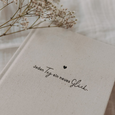 Detailaufnahme des Kalenders „Neues Glück“ mit Strukturcover und Schriftzug, dekoriert mit zarten Trockenblumen.