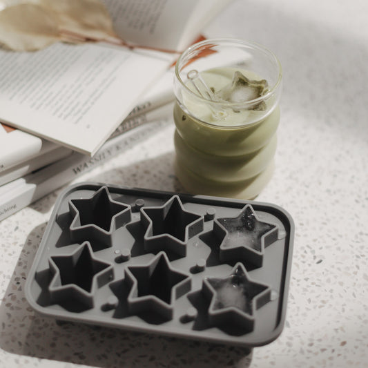 Matcha-Drink mit sternförmigen Eiswürfeln und Silikonform auf hellem Tisch mit Büchern.