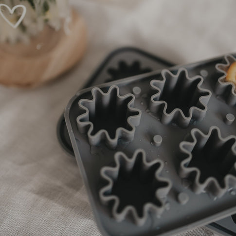 Nahaufnahme der grauen Blütenform aus flexiblem Silikon liegend auf einem Tisch mit Leinentischdecke.