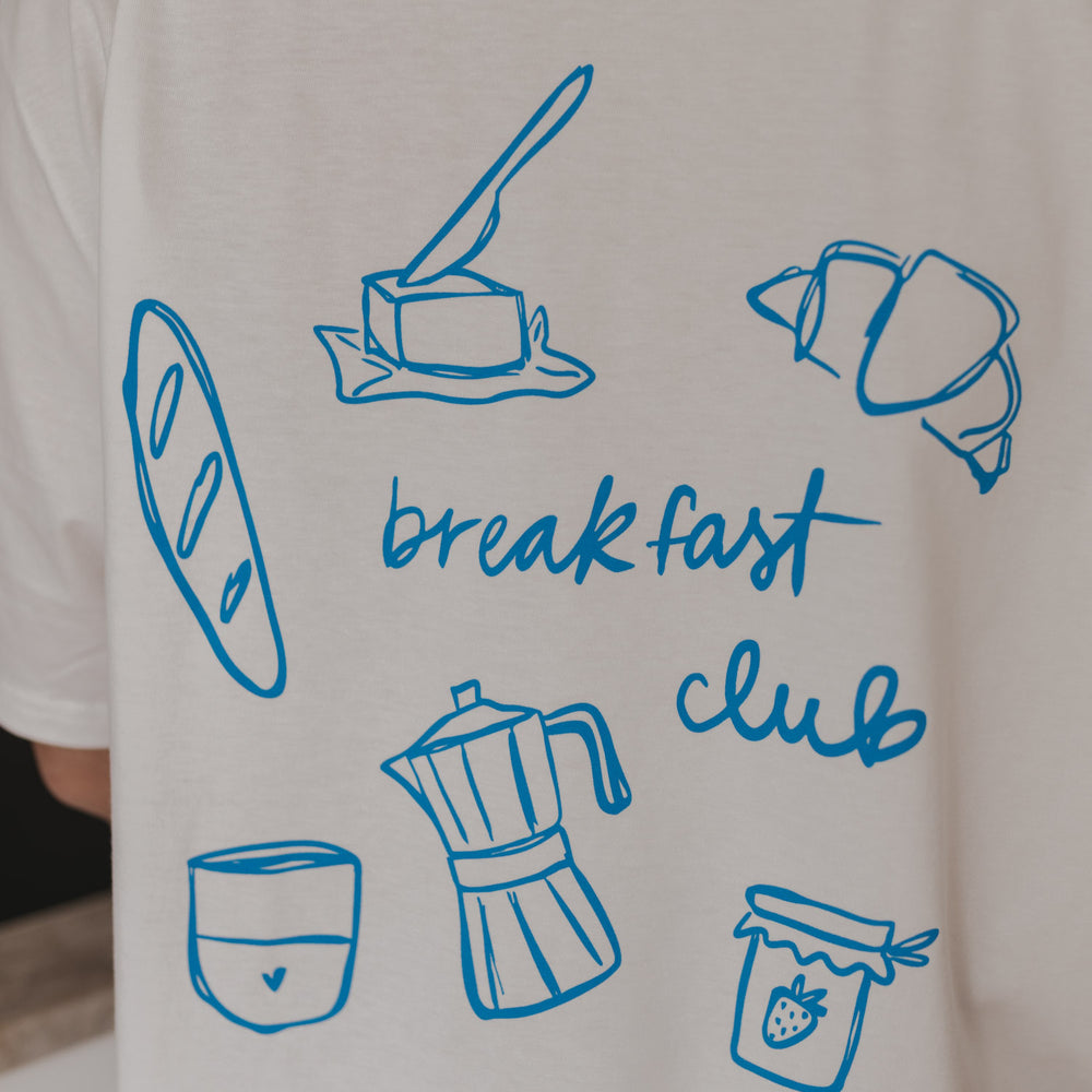 Nahaufnahme: Illustrationen von Croissant, Moka-Kanne und „breakfast club“-Schriftzug.