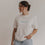 Frau trägt weißes Frühstücks-Shirt mit blauem Schriftzug, blickt seitlich in die Kamera.