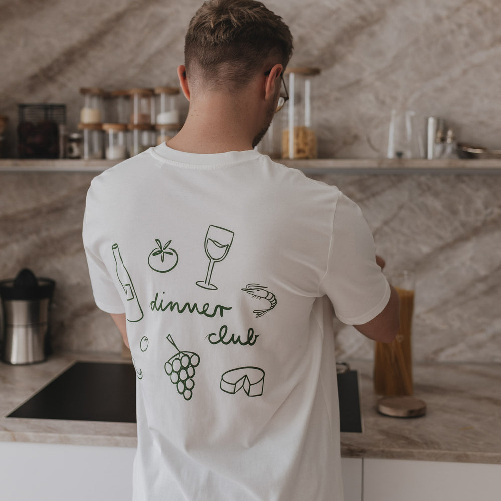 Rückansicht eines Mannes mit weißem Dinner Club Shirt und grünen Food-Icons in moderner Küche.