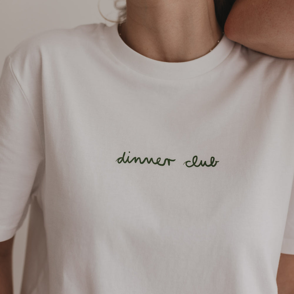 Nahaufnahme des Brustprints: grüner „dinner club“-Schriftzug auf weißem Shirt.