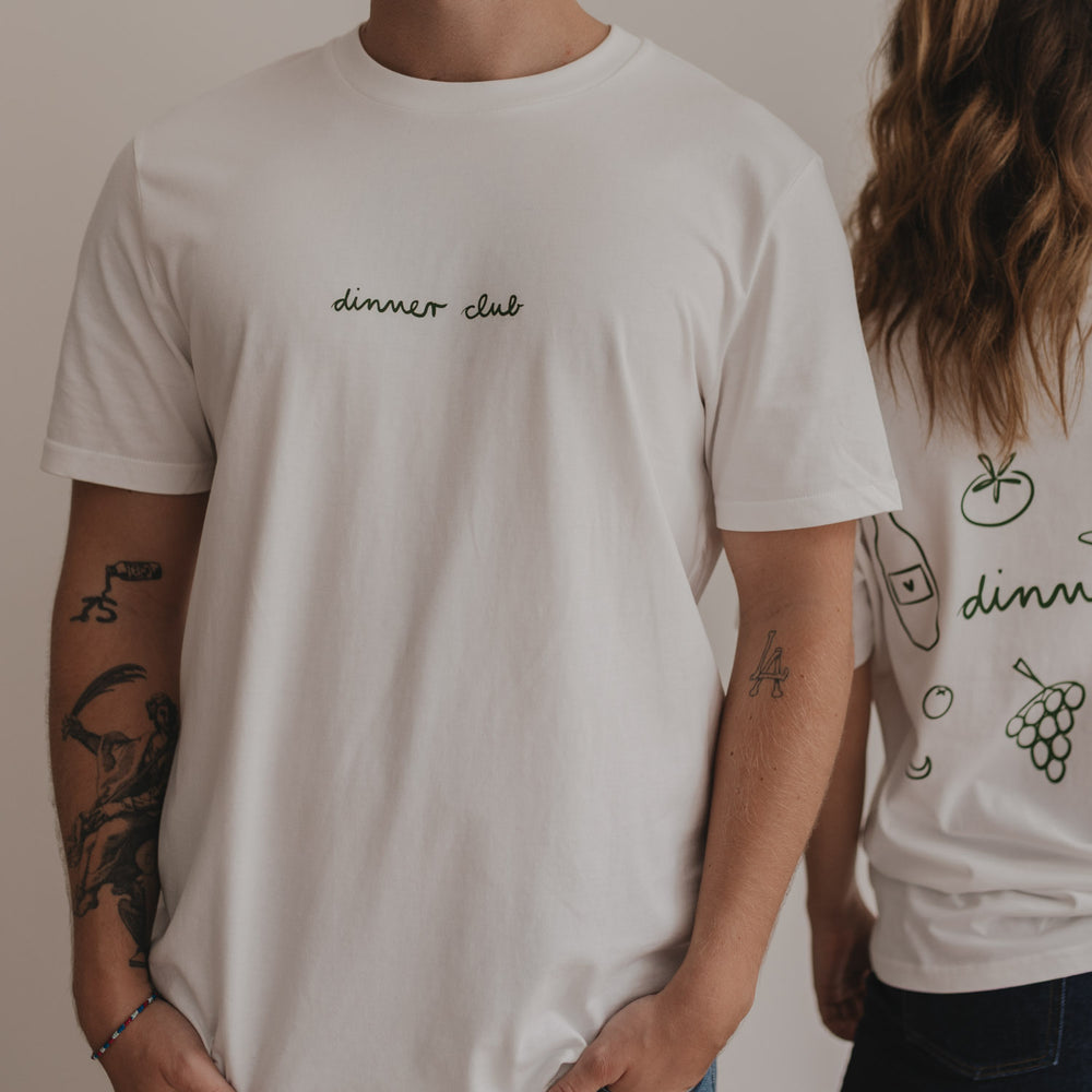 Fokus auf Frontdruck „dinner club“ in Grün, getragen von Person im weißen Shirt.