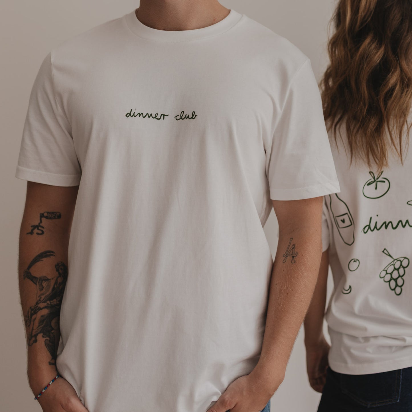 Fokus auf Frontdruck „dinner club“ in Grün, getragen von Person im weißen Shirt.