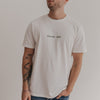 Mann trägt weißes Dinner Club Shirt mit grünem Schriftzug – schlichtes Frontdesign.