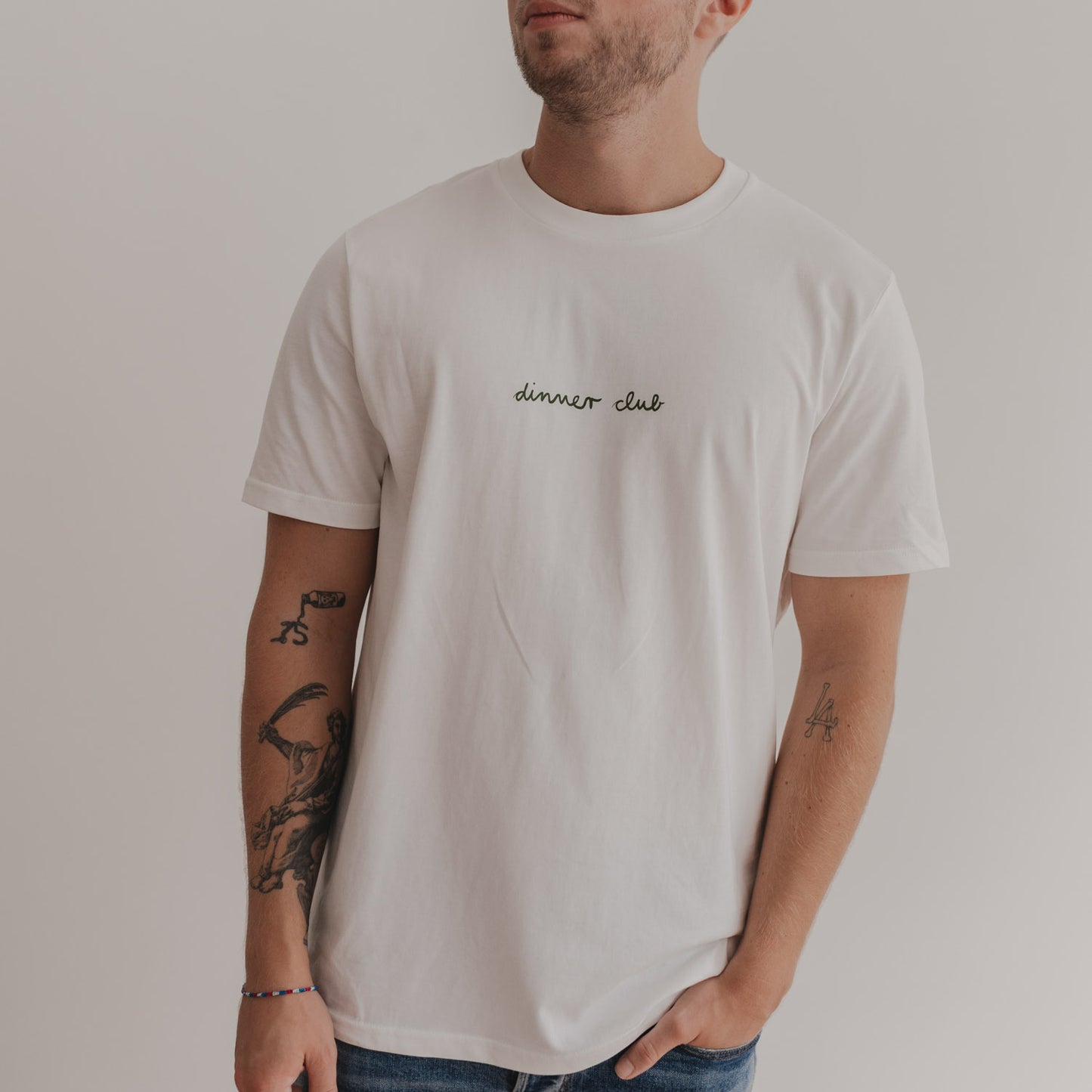 Mann trägt weißes Dinner Club Shirt mit grünem Schriftzug – schlichtes Frontdesign.