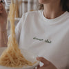 Weißes T-Shirt mit grünem „dinner club“-Schriftzug, getragen beim Servieren von Spaghetti.